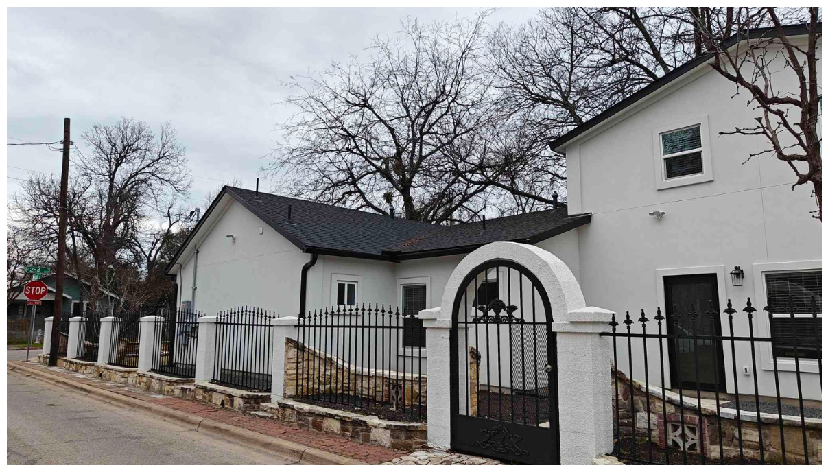 Unique corner view of Zeta House&#39;s white stucco exterior, featuring castle-like iron fences and gates, illustrating the architectural style of the property